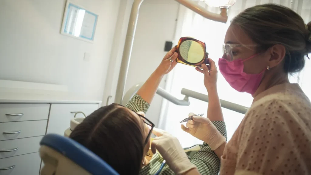 Paciente mira su sonrisa en un espejo de mano mientras la Dra. Analía Carrión la acompaña, en OdontoBa
